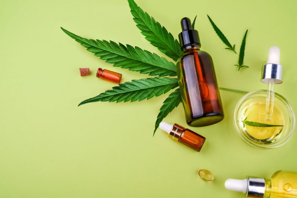 Different glass bottles with CBD OIL, THC tincture and cannabis leaves on yellow background. 